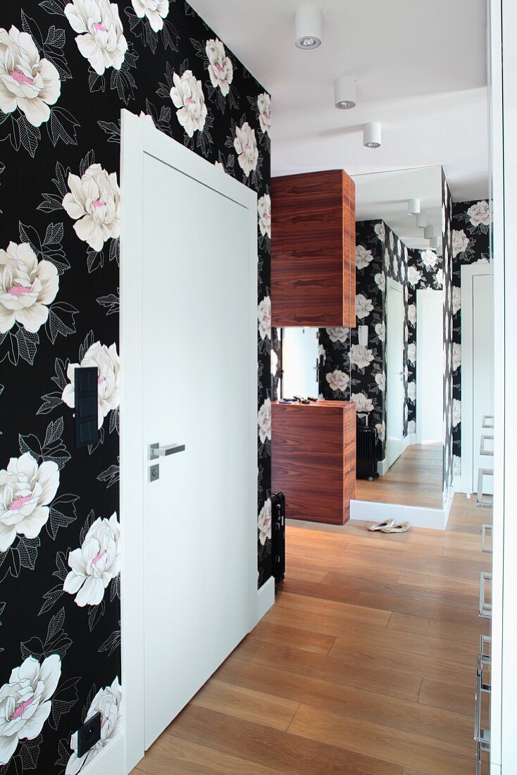 An elegant hallway hung with black and white floral paper with a mirror at the end