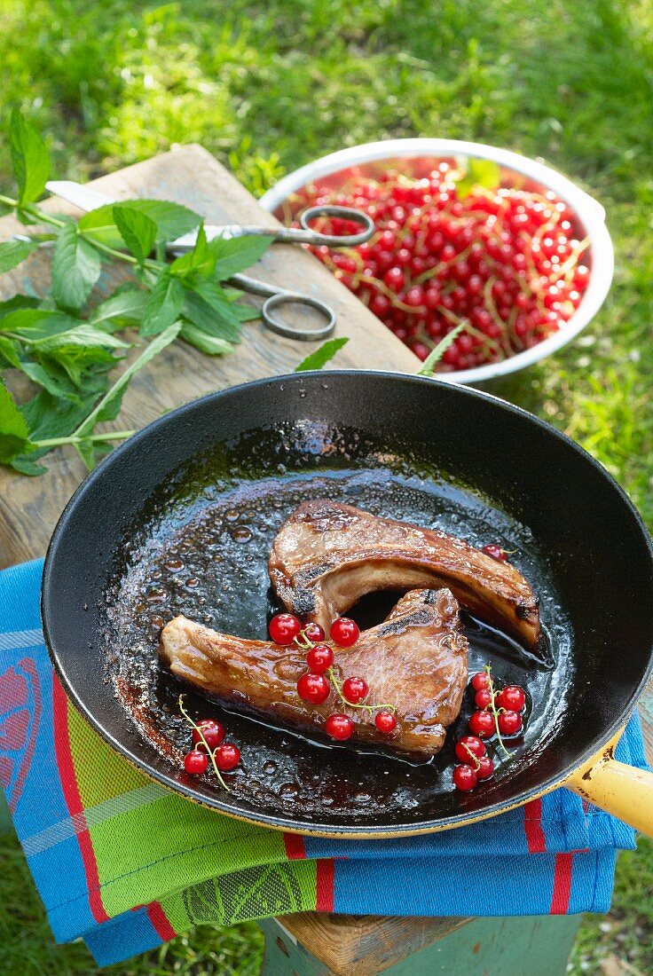 Two lamb chops with redcurrants in a frying pan on a garden table