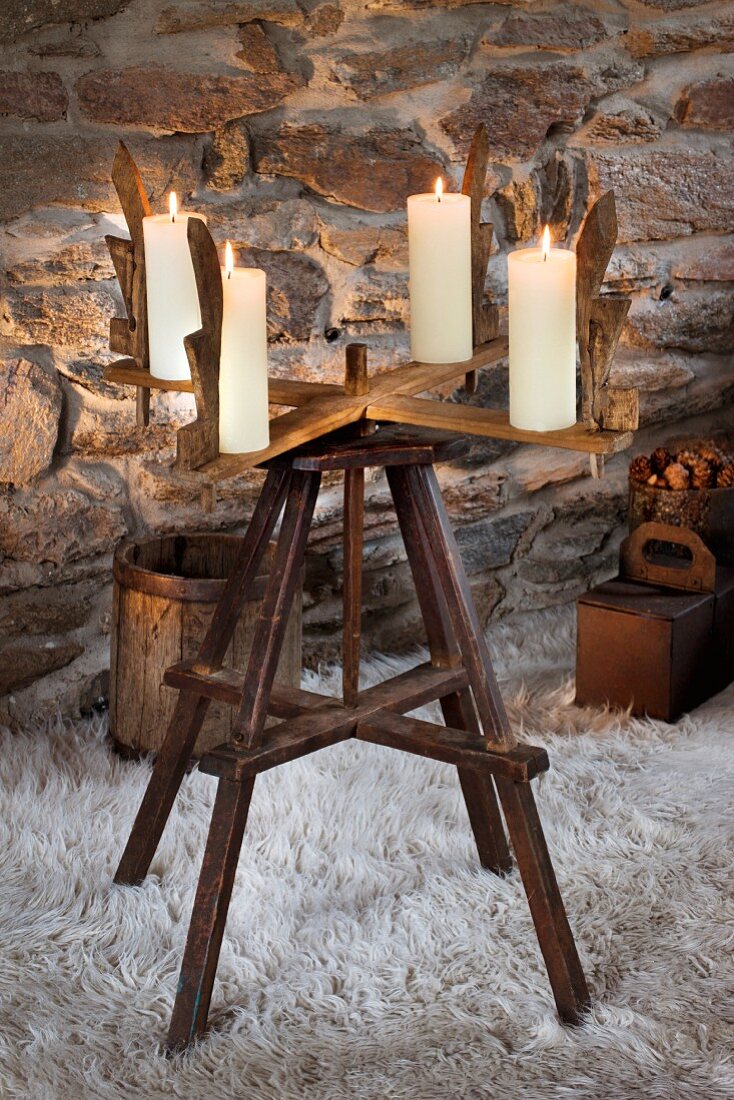 Old wooden reel with four candles used as Advent wreath on flokati rug in front of stone wall