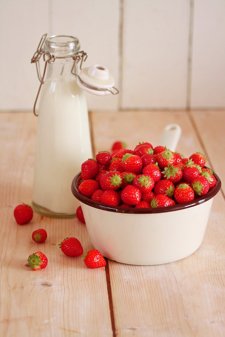 Strawberries in a saucepan next to a milk bottle