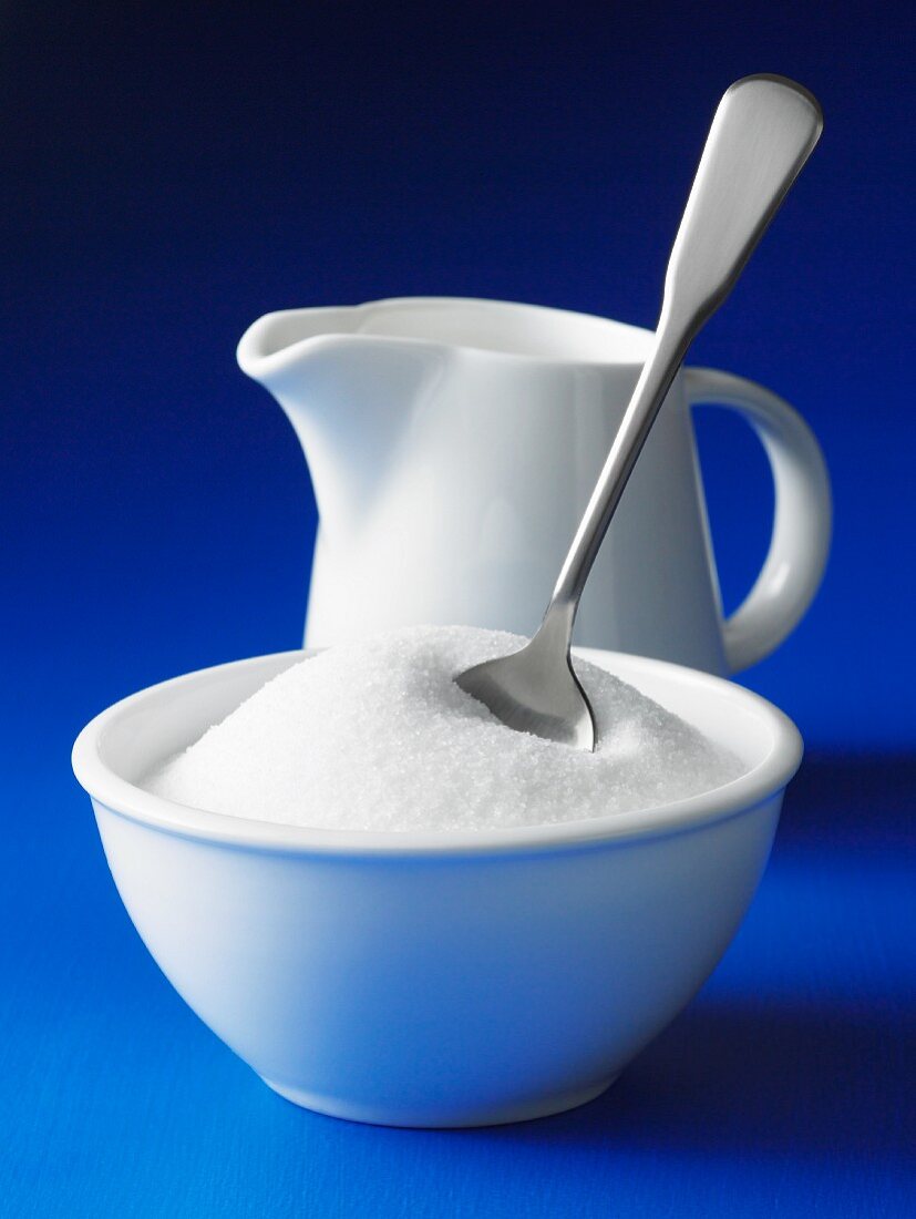 A bowl of sugar with a spoon and a jug of milk