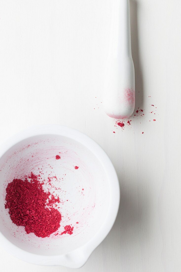Crushed dried raspberries in a white mortar with a pestle