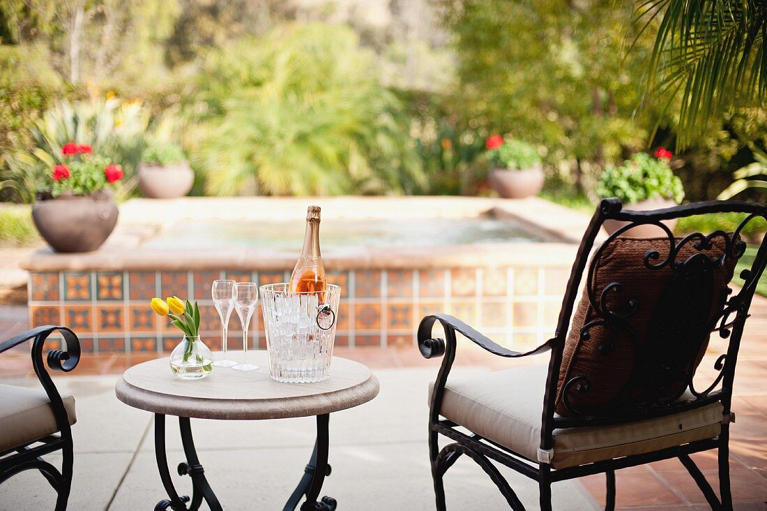 Flutes, vase and wine bottle in ice bucket on outdoor table against blurred plants