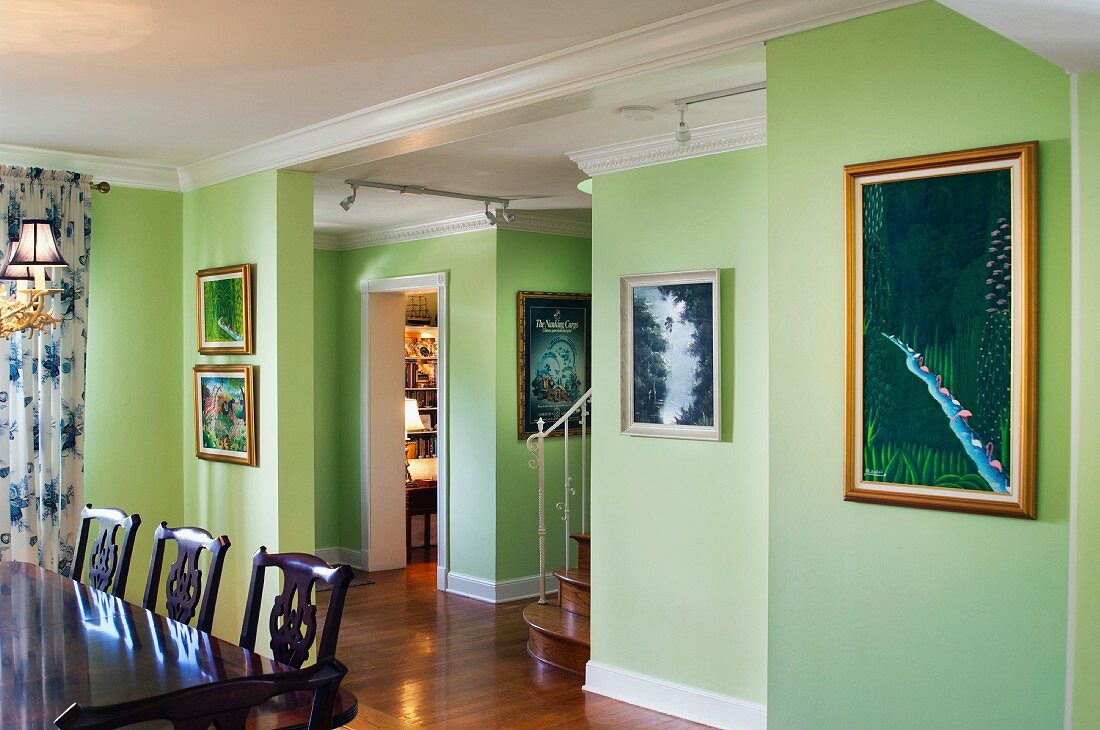 Cropped wooden dining table and chairs and paintings mounted on green walls; West Palm Beach; USA