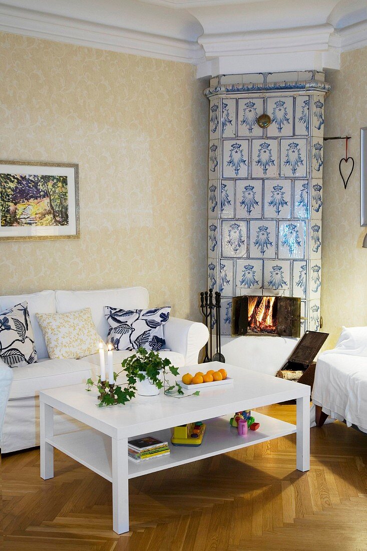 Cosy, country-house living room with stucco frieze and open fire in floor-to-ceiling tiled stove