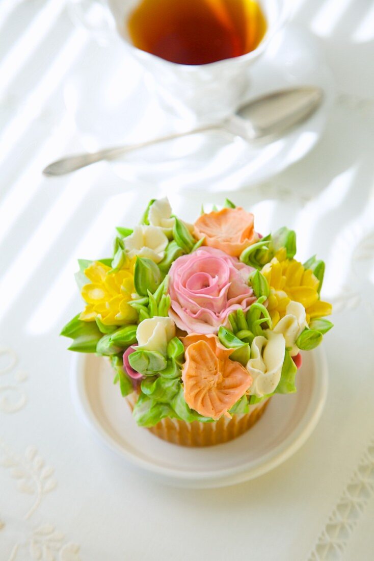 Cupcake mit romantischen Zuckerblumen vor Teetasse