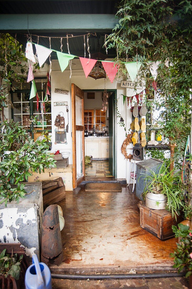 Vollgestellte Vintage-Terrasse, geschmückt mit Stoff-Wimpelkette und Blick in die Küche