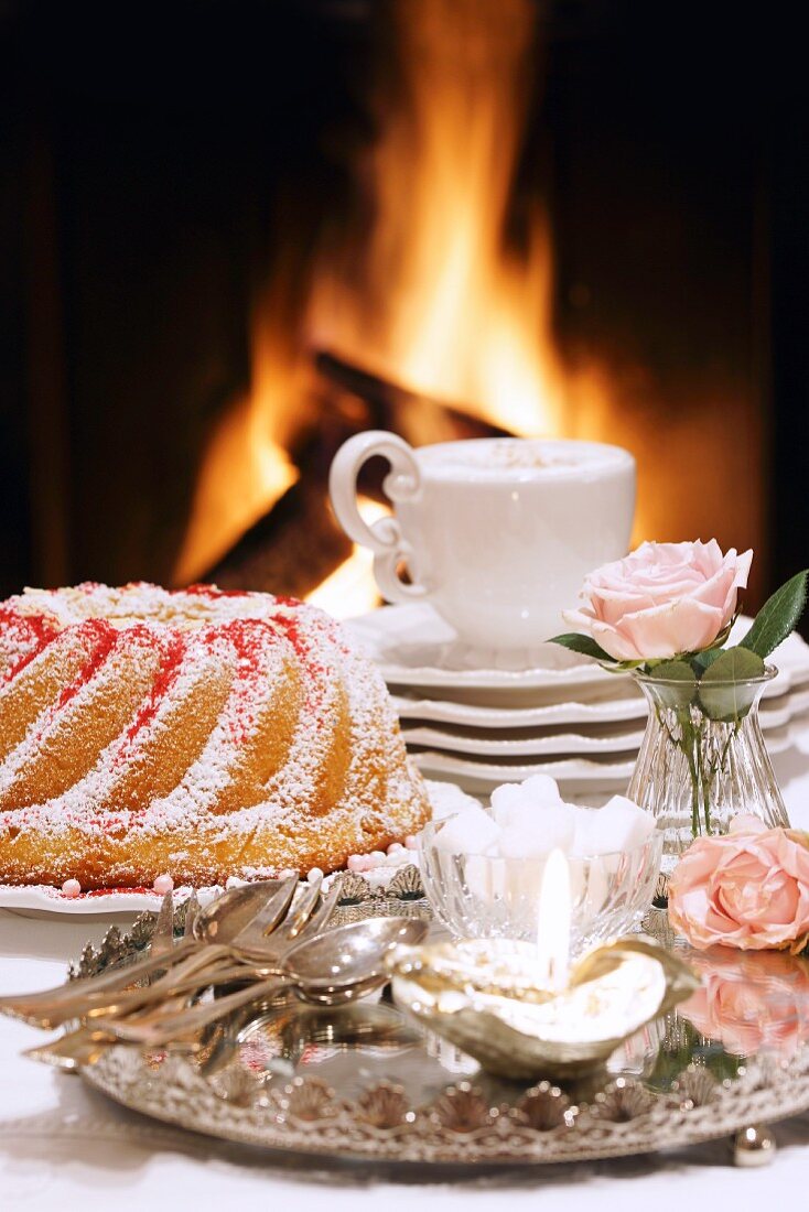 A Bundt cake and a cappuccino in front of an open fire