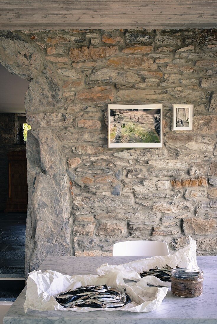 Fresh fish wrapped in paper on marble table with small pictures on rustic stone wall in background