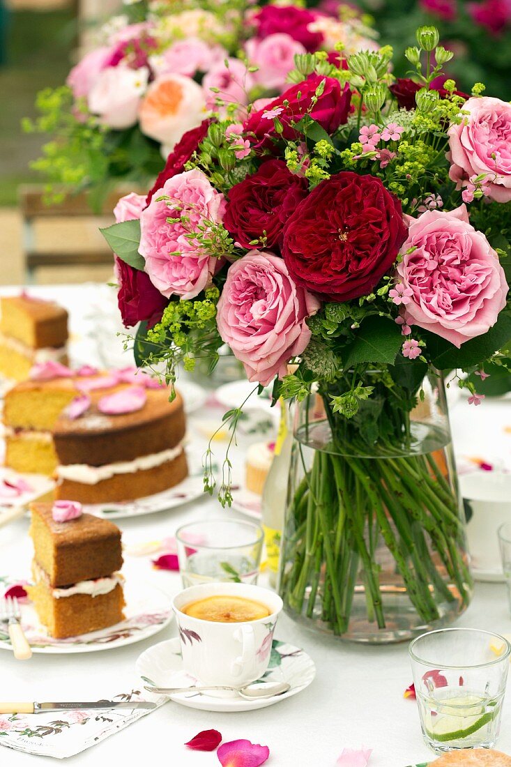 Bouquet of summer flowers on set table with cake and cups of coffee