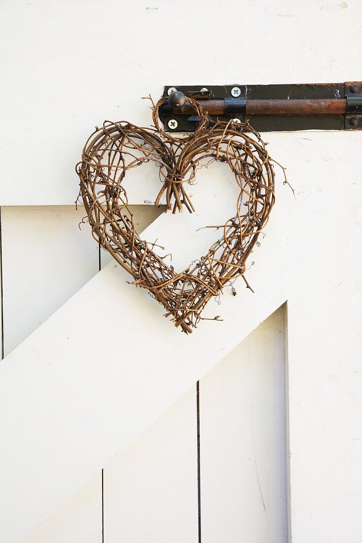Herzförmiger Kranz aus Weidenzweigen an Riegel einer Holzwand aufgehängt