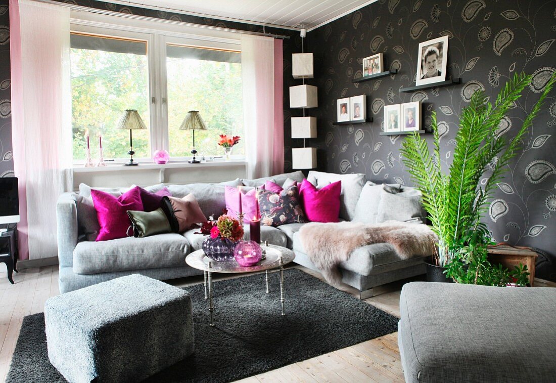 Comfortable corner sofa, grey patterned wallpaper, hot pink scatter cushions and family photos on wall