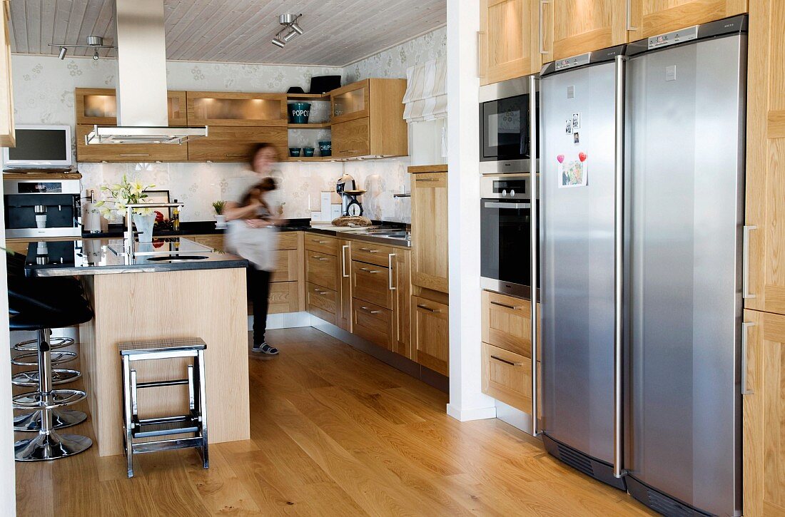 Spacious open-plan kitchen with wooden fronts and parquet floor; modern, black bar stools with stainless steel bases at kitchen counter