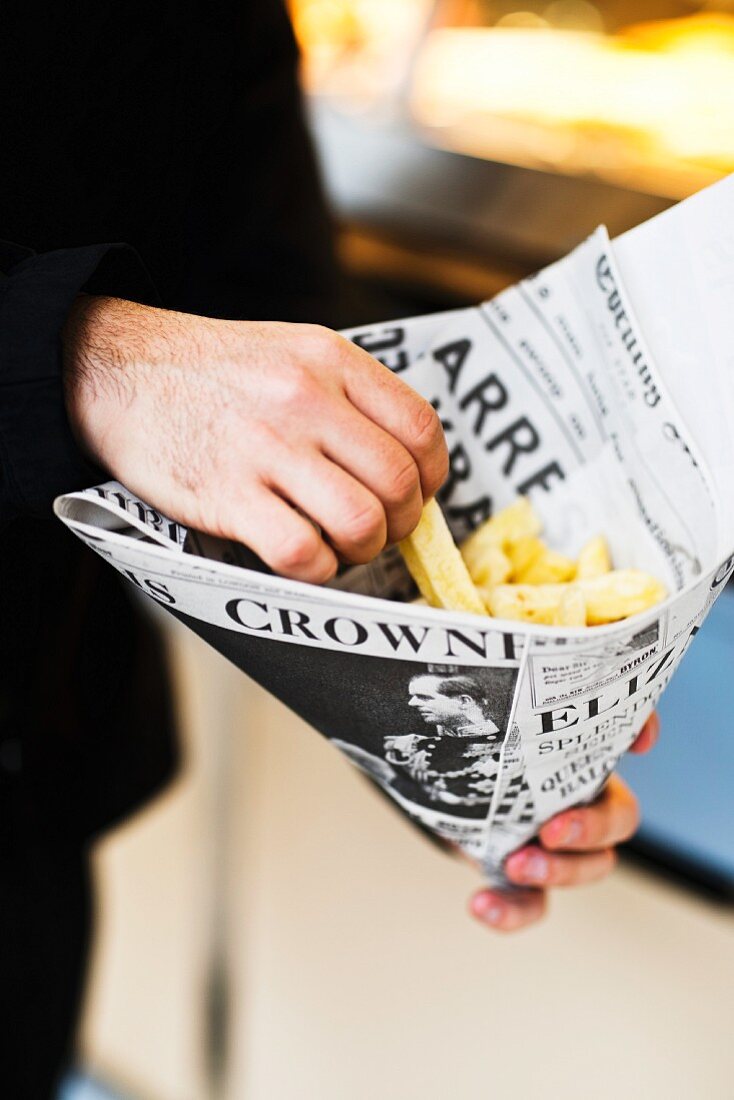 A man holding a newspaper cone of fish and chips
