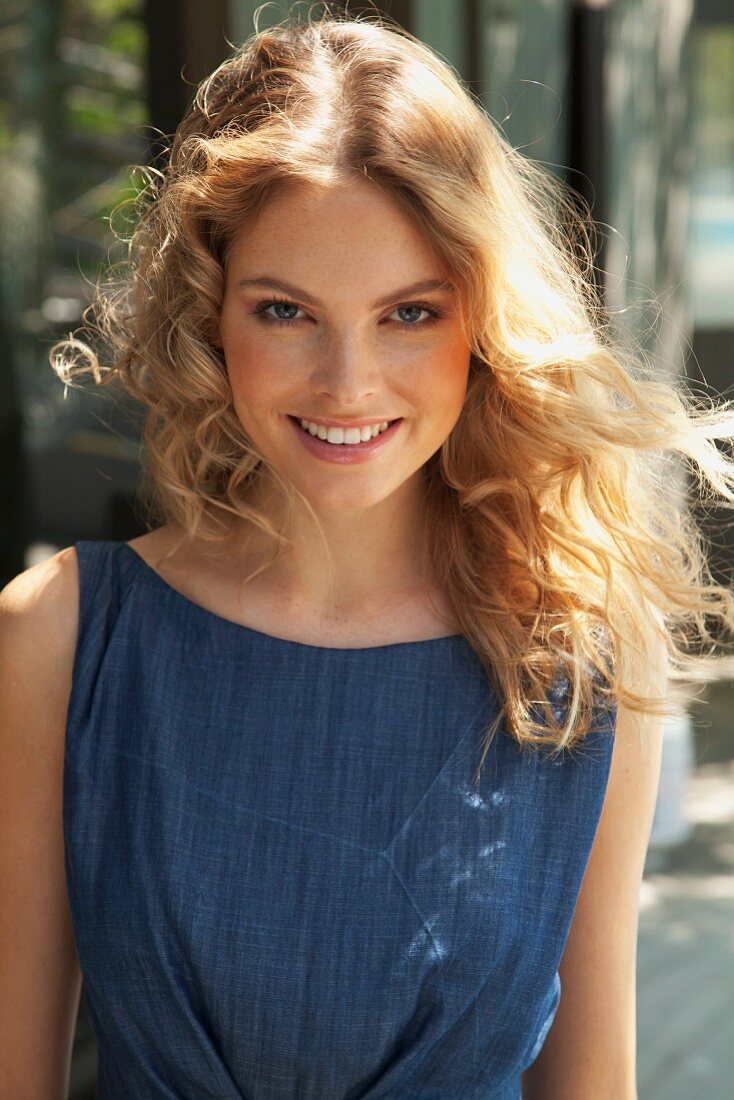 A young blonde woman outside wearing a blue summer dress
