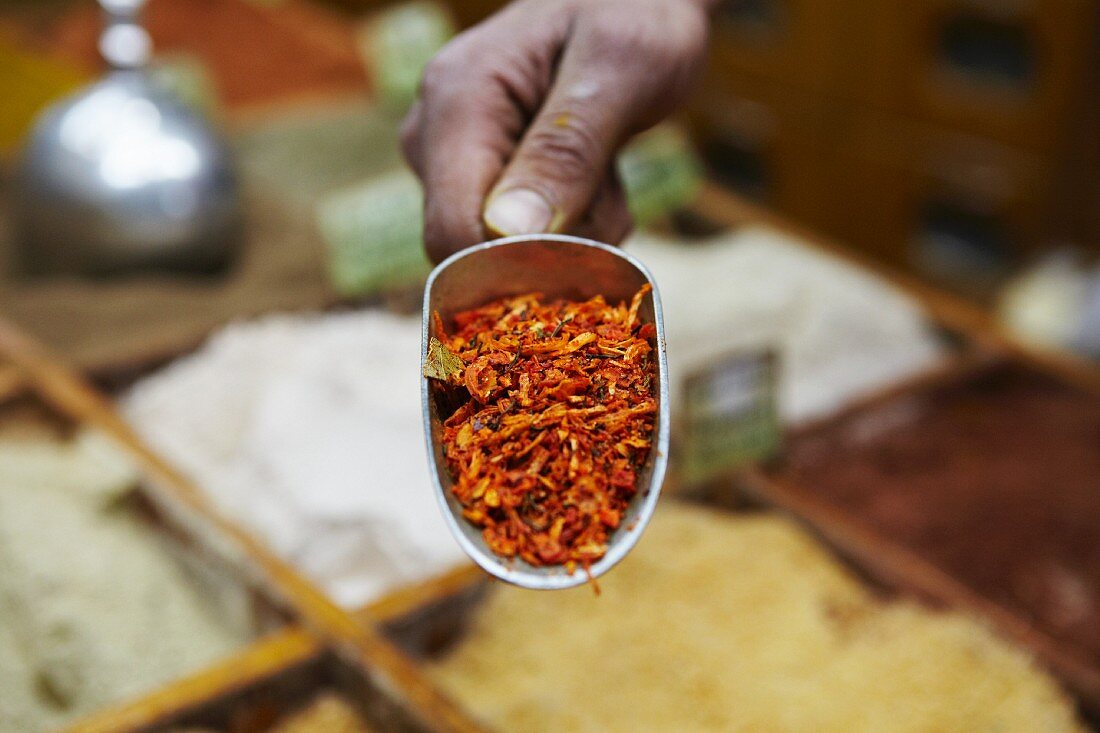 A hand holding a scoop of kabseh spice mix at a market