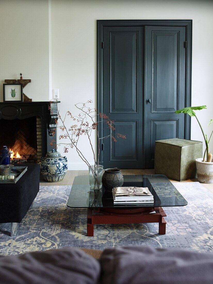 Low coffee table with smoked glass top on vintage-look rug in front of double doors painted dark grey