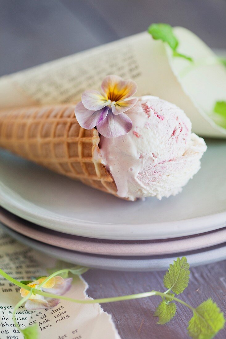 Strawberry ice cream in a cone decorated with pansies on a stack of plates