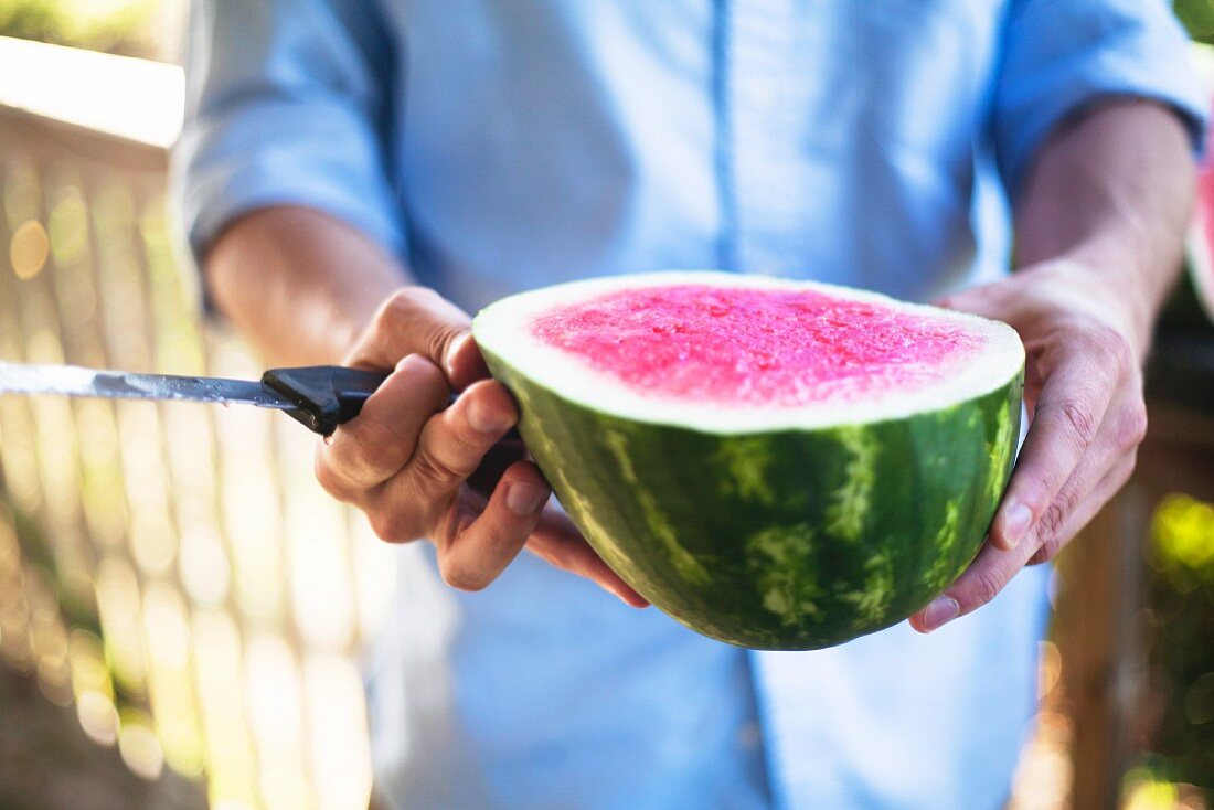 A man holding a halved watermelon and a knife