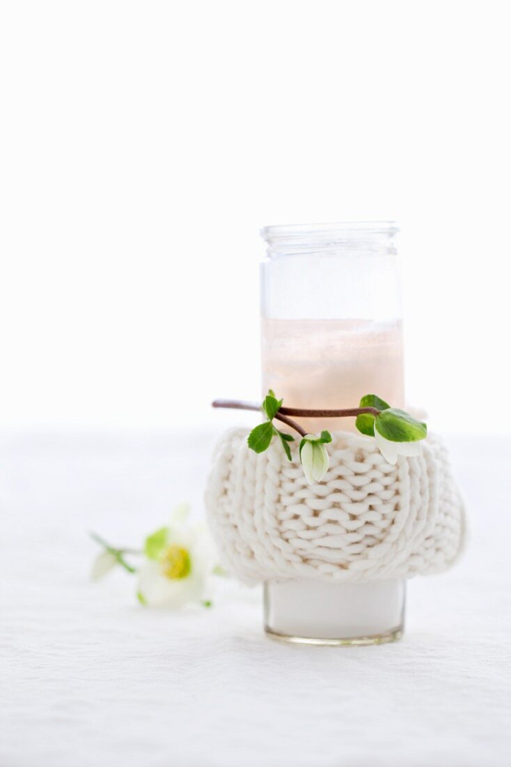 A candle in a glass with a knitted cover