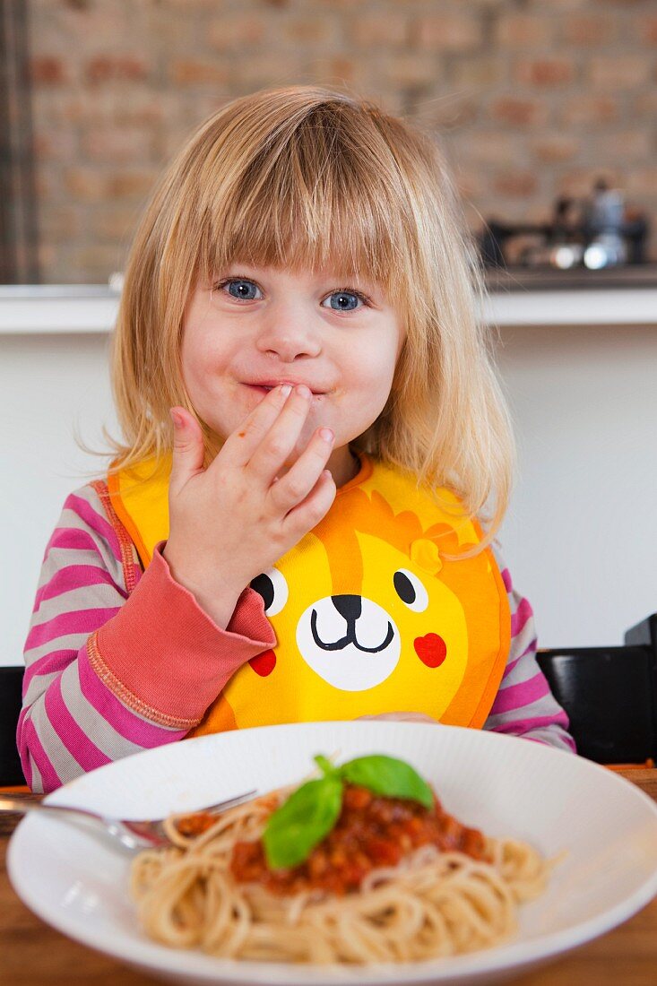 Kleines blondes Mädchen probiert Spaghetti Bolognese mit den Fingern