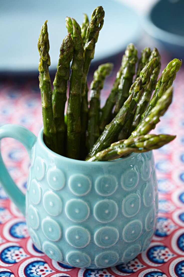 Cooked green asparagus in a light blue, ceramic mug