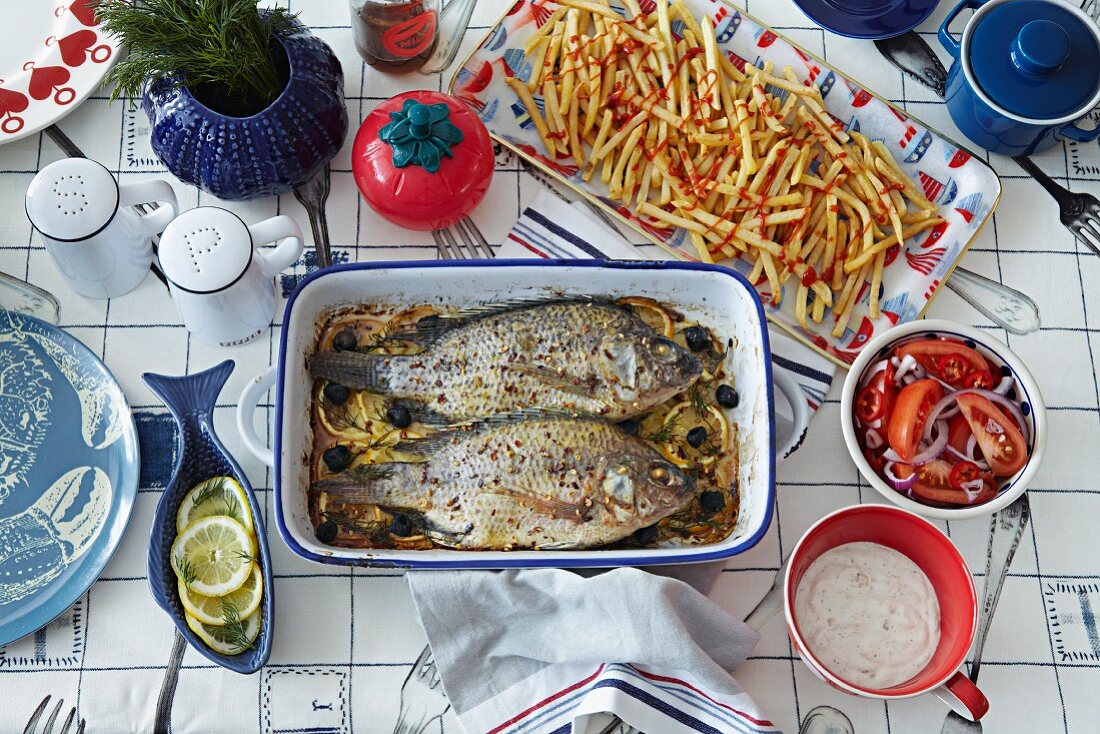 Blick auf Tisch mit zwei gebratenen Fischen in Reine, Pommes Frites und Salat