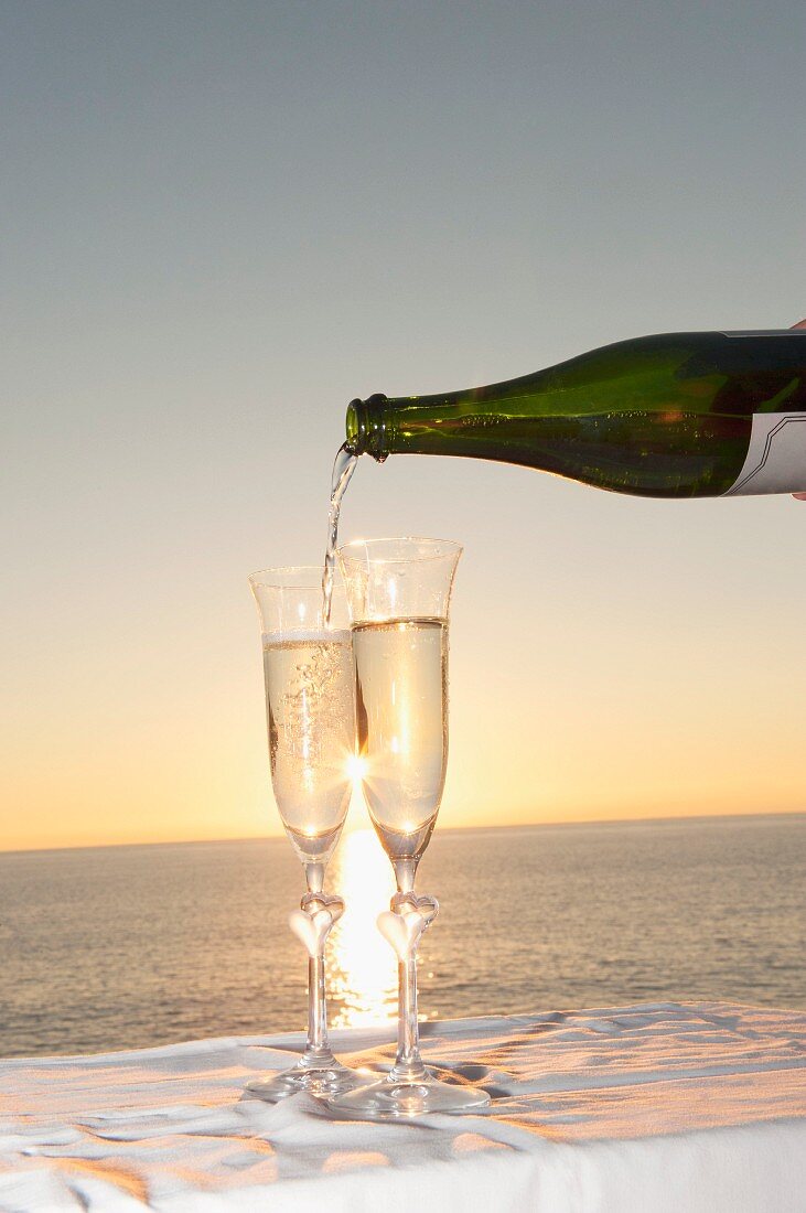 Champagner wird in Flöten vor Sonnenuntergang am Meer gegossen