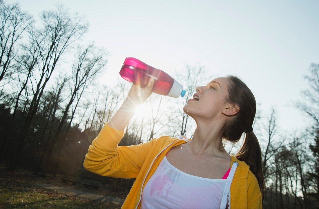 A young female runner drinking from a water bottle