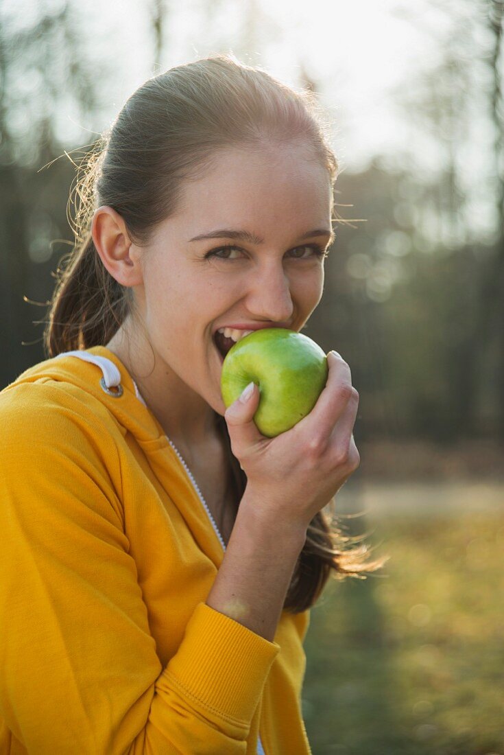 A young brunette woman biting into a green apple