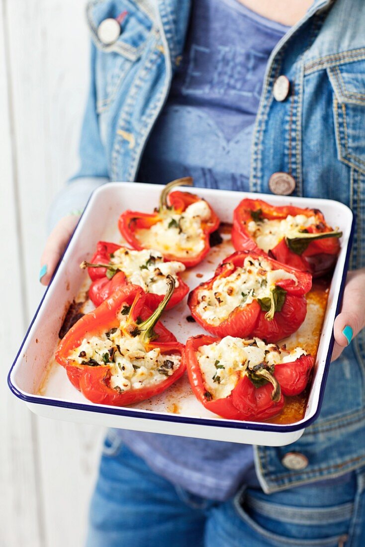 A woman holding peppers stuffed with feta and mozzarella on a baking tray