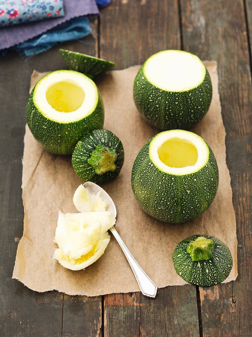 Hollowed-out, round courgettes on a piece of baking paper