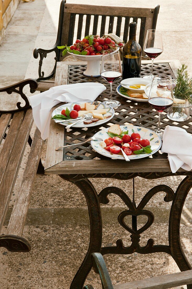 A patio table laid with plates of salad and red wine