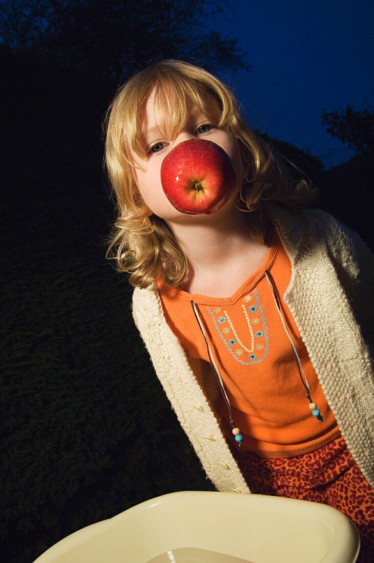 A little girl holding an apple between her teeth