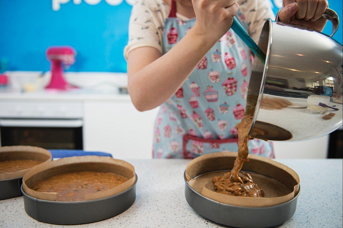 Frau gießt flüssigen Teig in Kuchenformen in einer Bäckerei