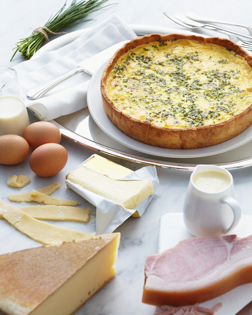 A freshly baked quiche Lorraine with the ingredients in the foreground