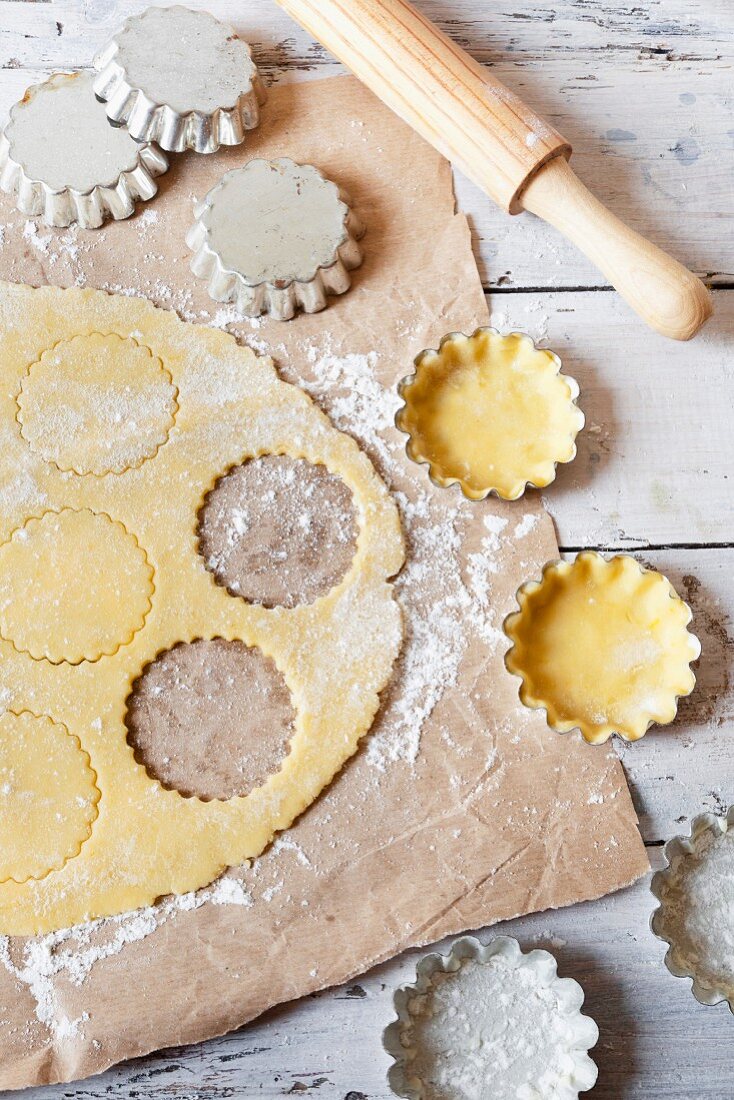 Shortcrust pastry on a work surface and in metal tins with a rolling pin