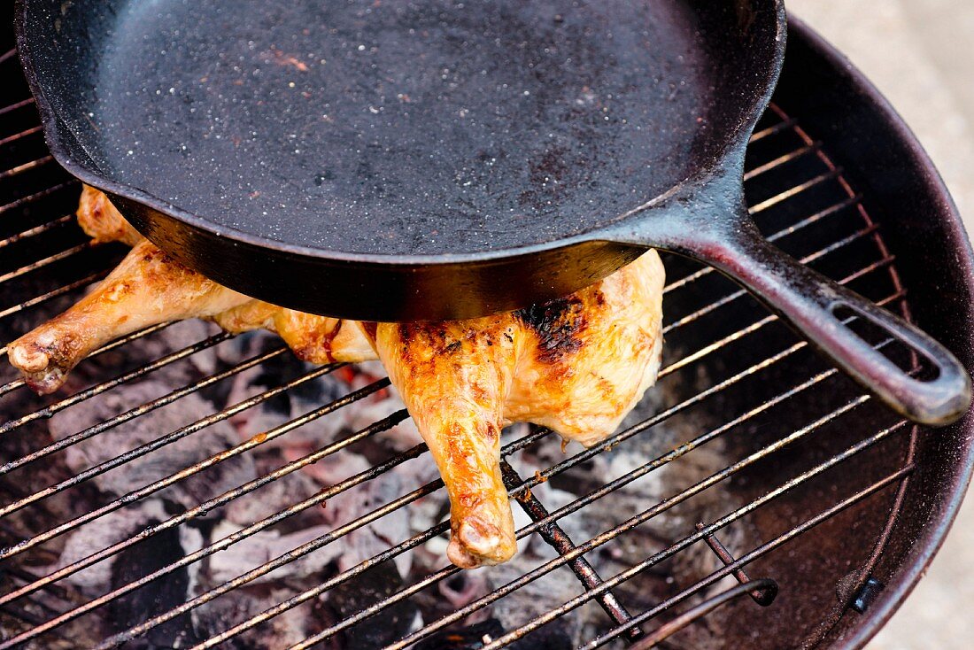 Hähnchen auf dem Grill mit Pfanne beschweren