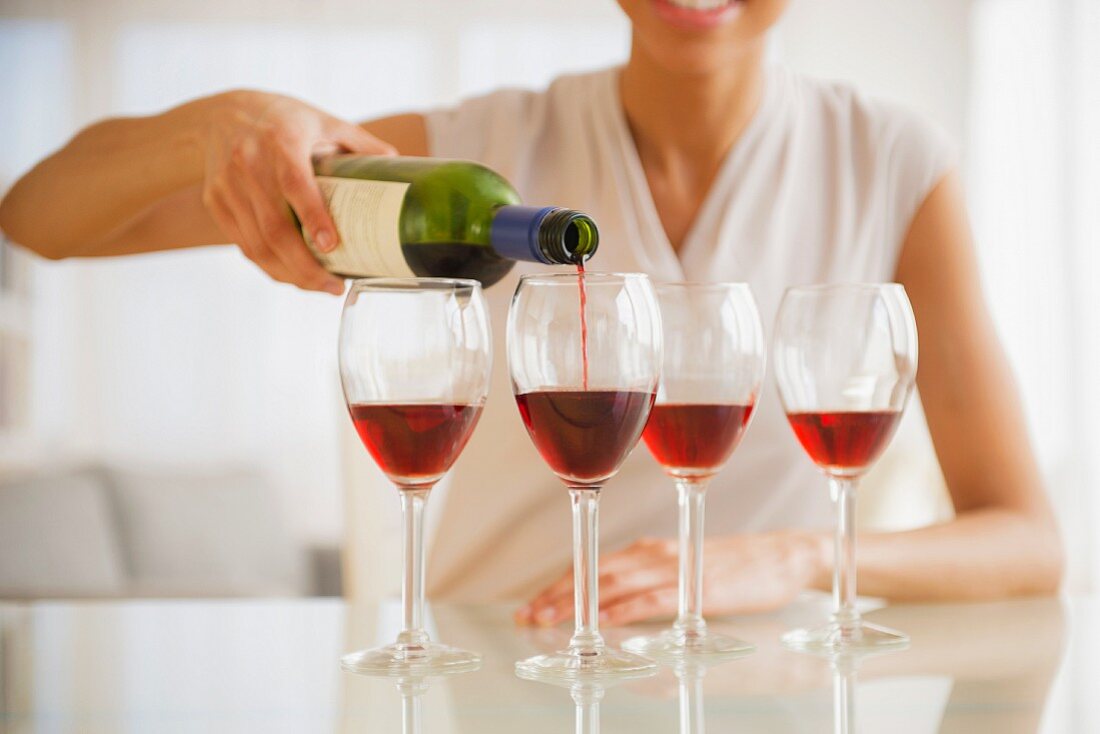 A woman pouring red wine into four glasses