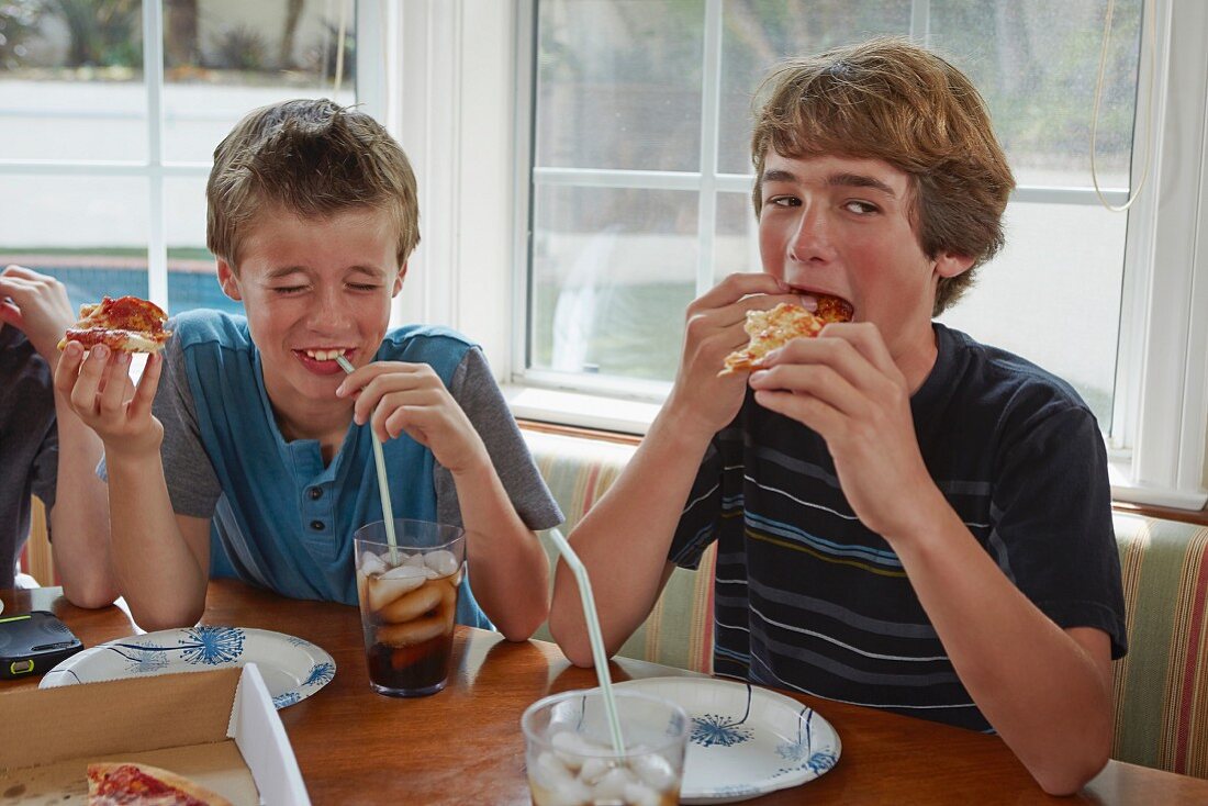 Boys eating pizza and drinking cola in a kitchen