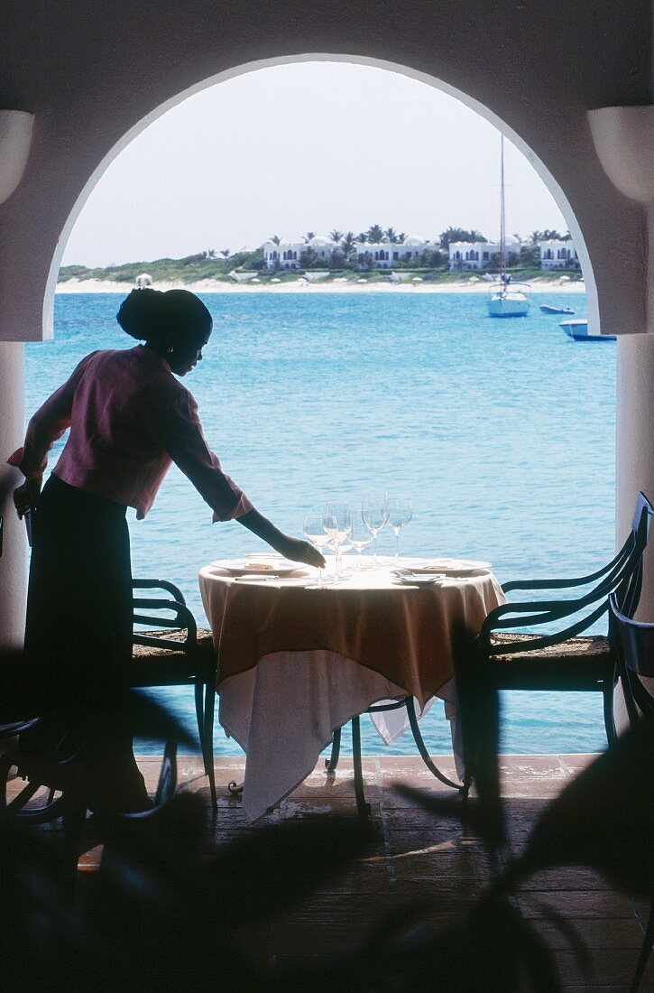 A young woman placing glasses on a restaurant table with a seaview