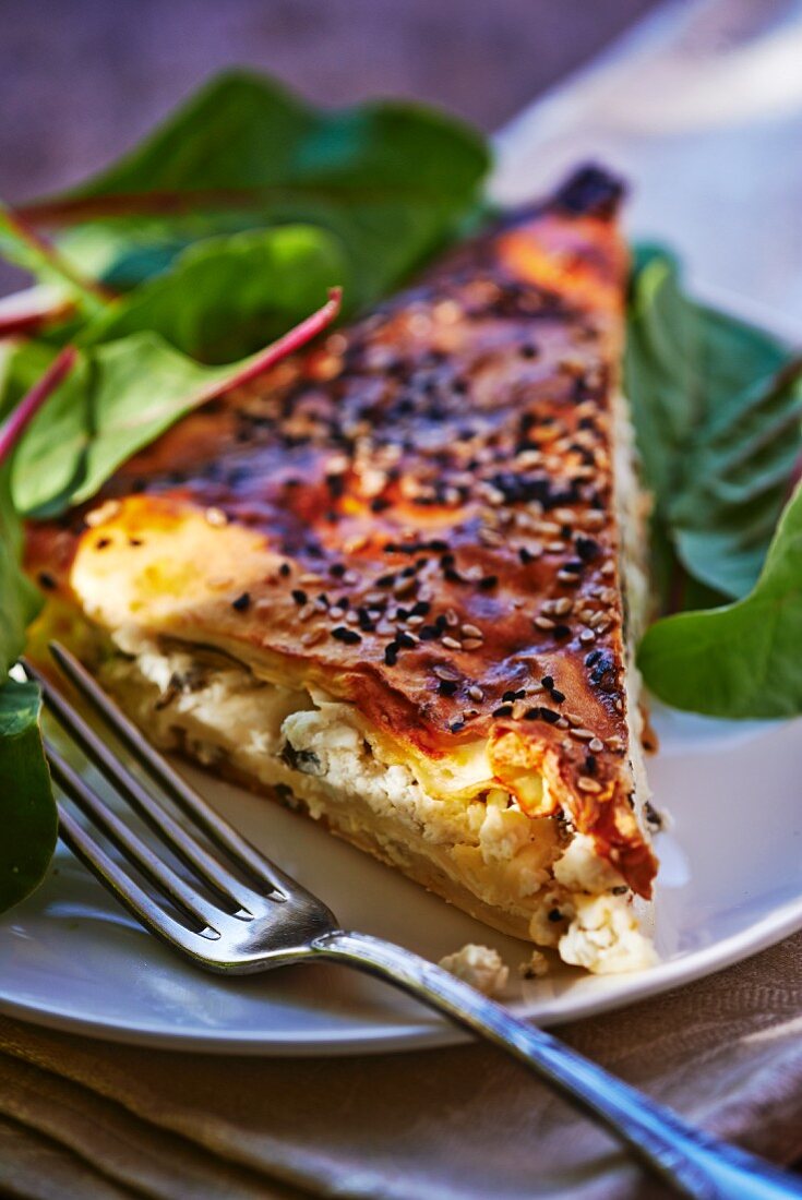 A slice of puff pastry tart with sesame seeds and feta cheese