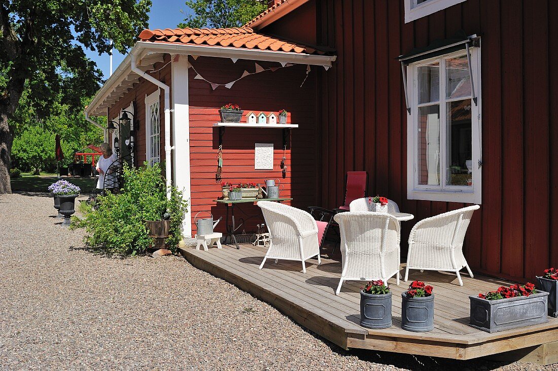 Sunny terrace with white wicker armchairs and vintage planters outside traditional Swedish house