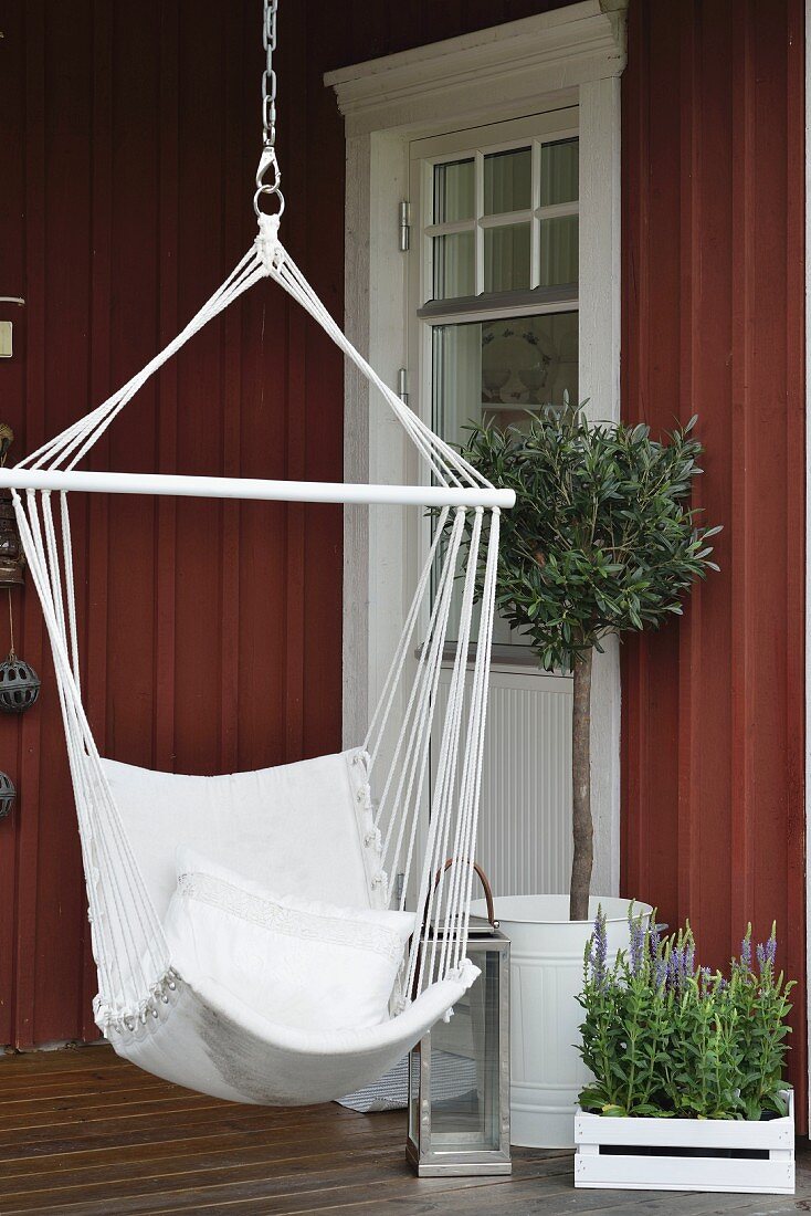 Hammock chair next to lantern and olive tree on veranda of Swedish house