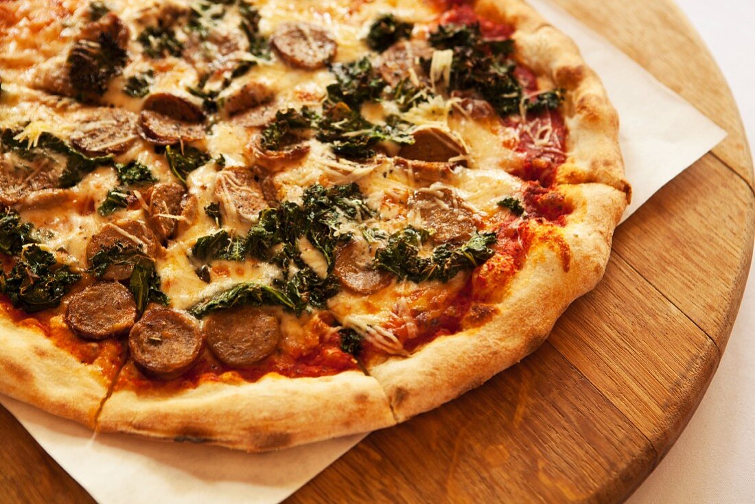 A pizza topped with wild boar sausage, braised green kale and smoked mozzarella cheese