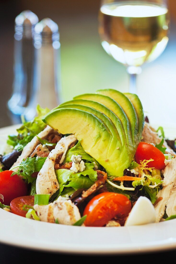 Cobb salad with avocado, tomatoes, bacon and chicken served with a glass of wine