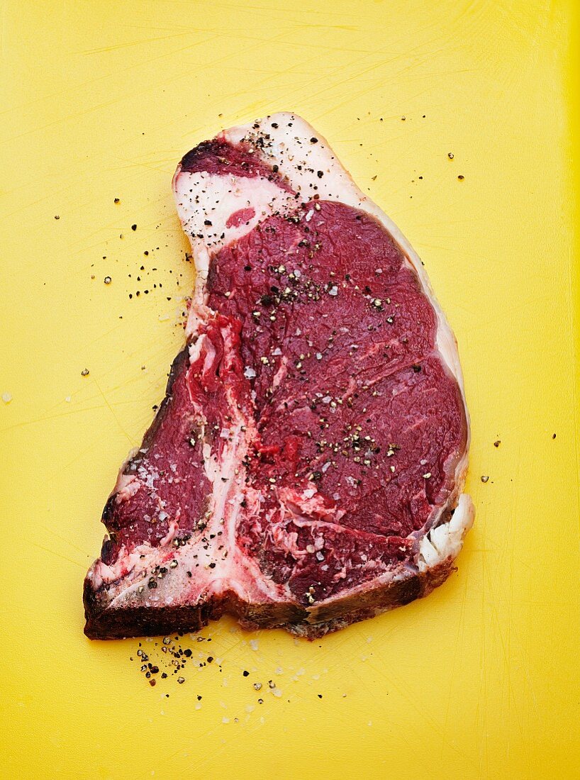A raw T-bone steak seasoned with salt and pepper