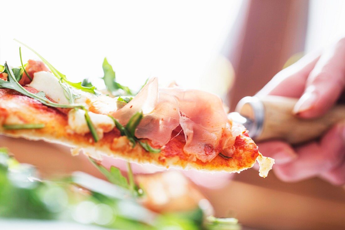 A close up of a slice of pizza with Parma ham and rocket on a server