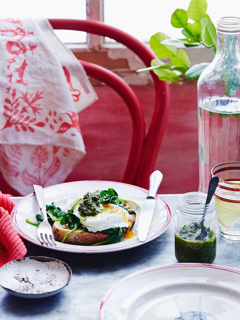 A poached egg and spinach sandwich served with pesto and water on a table