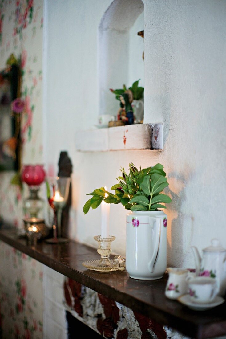 Auf Kaminsims Porzellankanne mit Blätterzweigen und Kaffeeservice, darüber kleine Nische in Wand